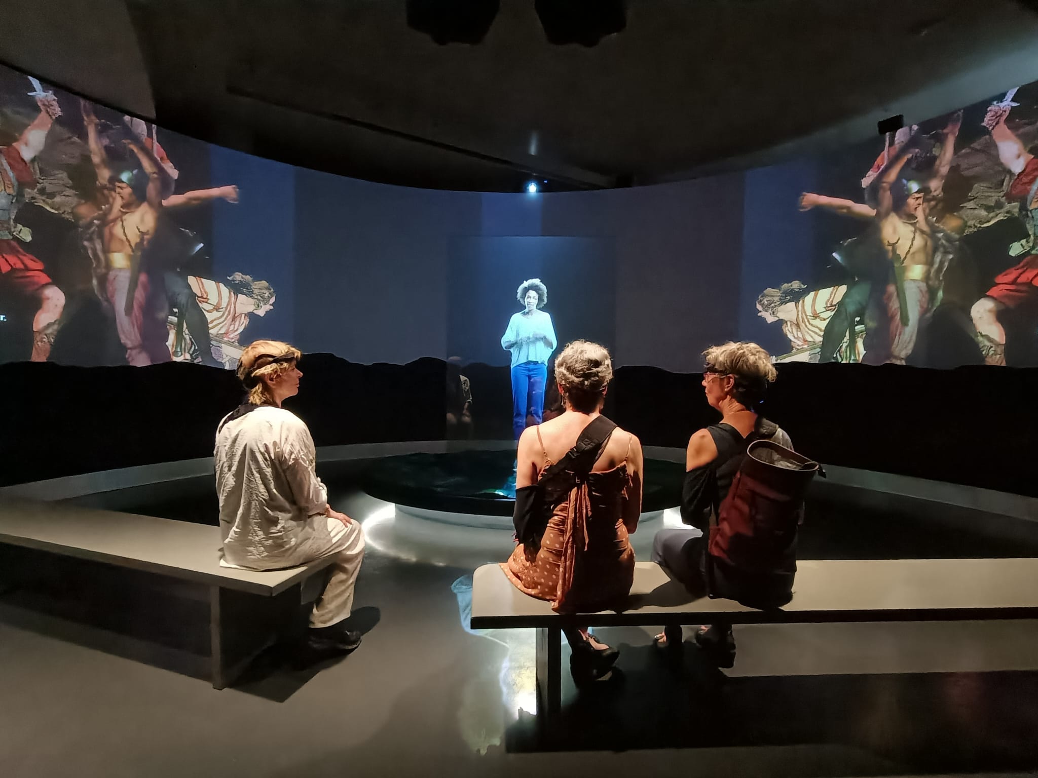 three people sitting on a bench in a room and watching video screening.